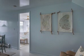 A room with a light blue wall, a bed with white bedding, a wooden chair, and two wall-mounted tapestries. - Designer Waterfront Newly Renovated Cottage "ROXABOXEN" (Tremont)