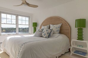 Ein Schlafzimmer mit einem großen Bett, Blick ins Freie und einem Deckenventilator.