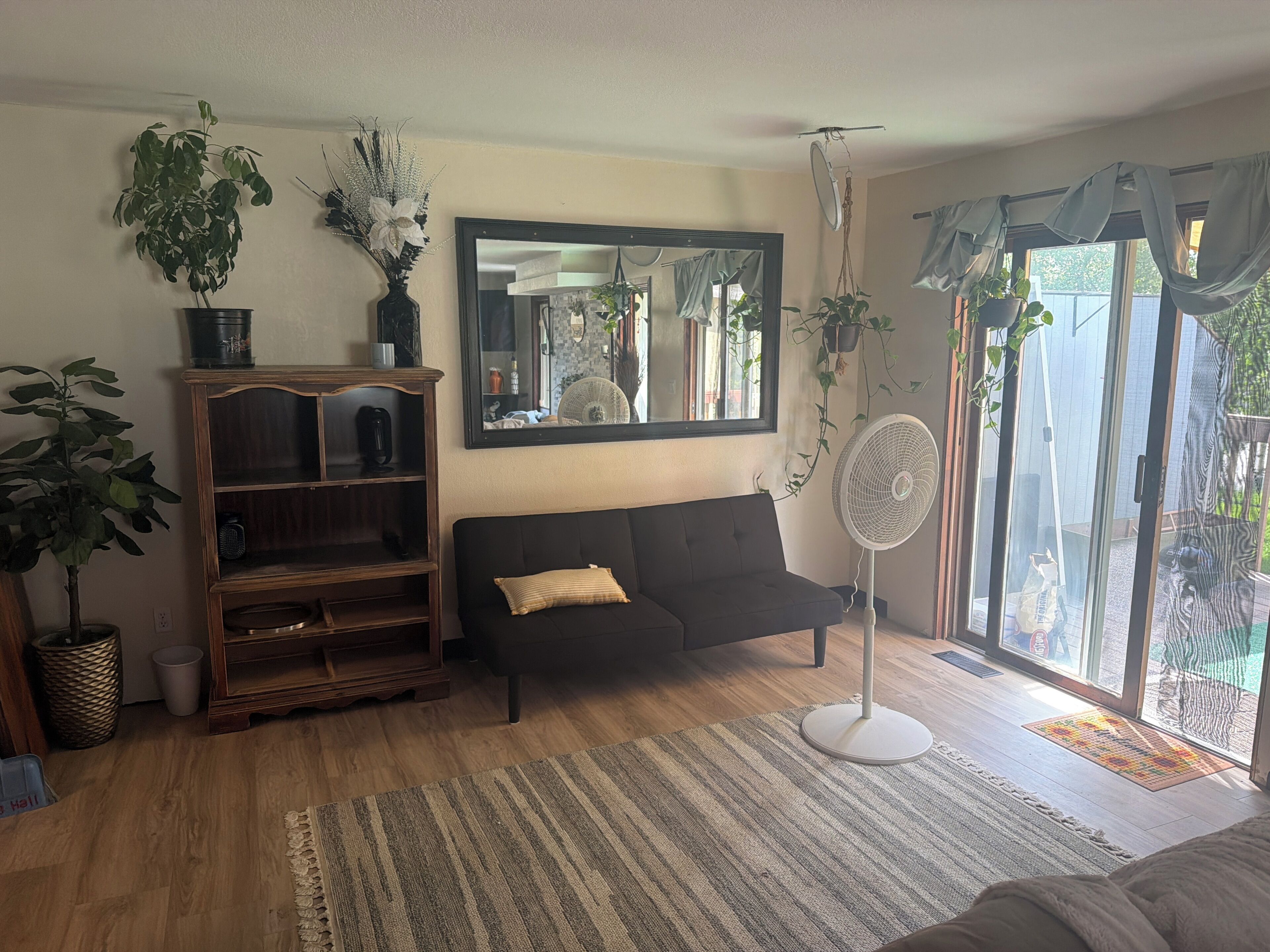 A living room with a sofa, a wooden entertainment unit, a large mirror, and a fan.