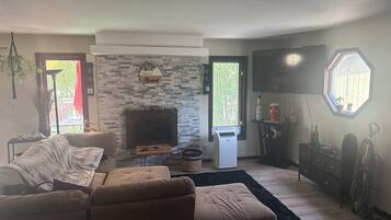 A living room with a fireplace, a sofa, a TV, and a window with a view of trees.