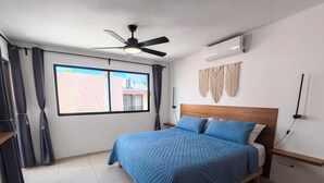 Een slaapkamer met een bed, een plafondventilator, een airconditioning, een raam met gordijnen en een wandlamp.