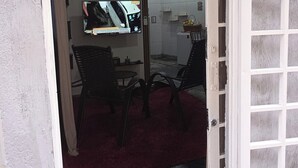 An open door leading to a room with a television, a table, chairs, and a red mat on the floor. - Studio apartment near the shopping mall. (Campo Grande)