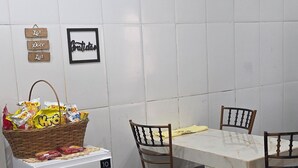 A compact kitchen with a white refrigerator, a dining table with four chairs, and a tiled backsplash. - Studio apartment near the shopping mall. (Campo Grande)