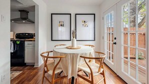 Een eetruimte met een ronde tafel, stoelen, een lijst met kunst aan de muur en uitzicht door een glazen deur.
