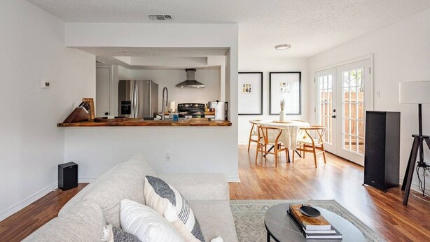 Een moderne woonkamer met een bank, een eethoek met een tafel en stoelen, een keuken met een fornuis en een koelkast, en een groot raam met uitzicht.
