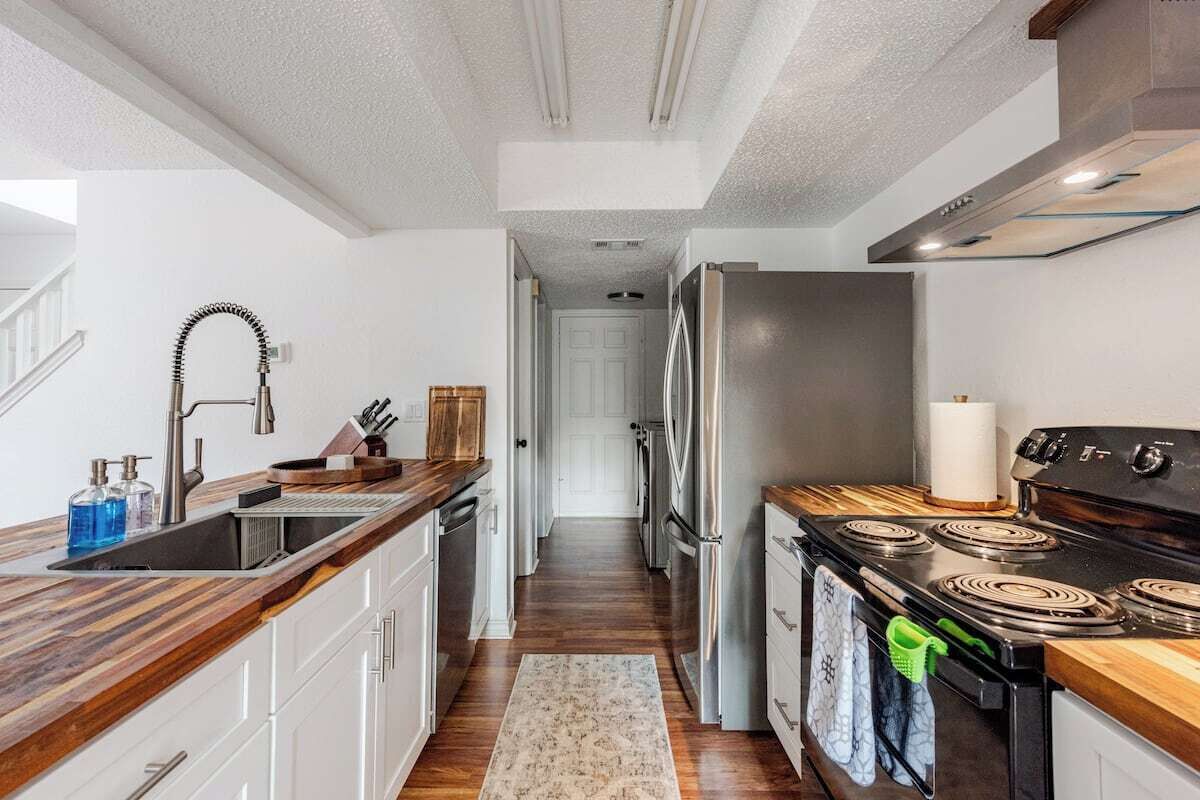 Une cuisine moderne avec un réfrigérateur en acier inoxydable, une cuisinière noire et un plan de travail en bois.