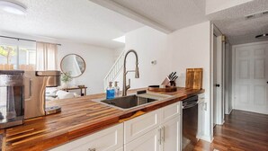 Een keuken met een houten aanrechtblad, witte kasten, een roestvrijstalen spoelbak en een afwasschaal.