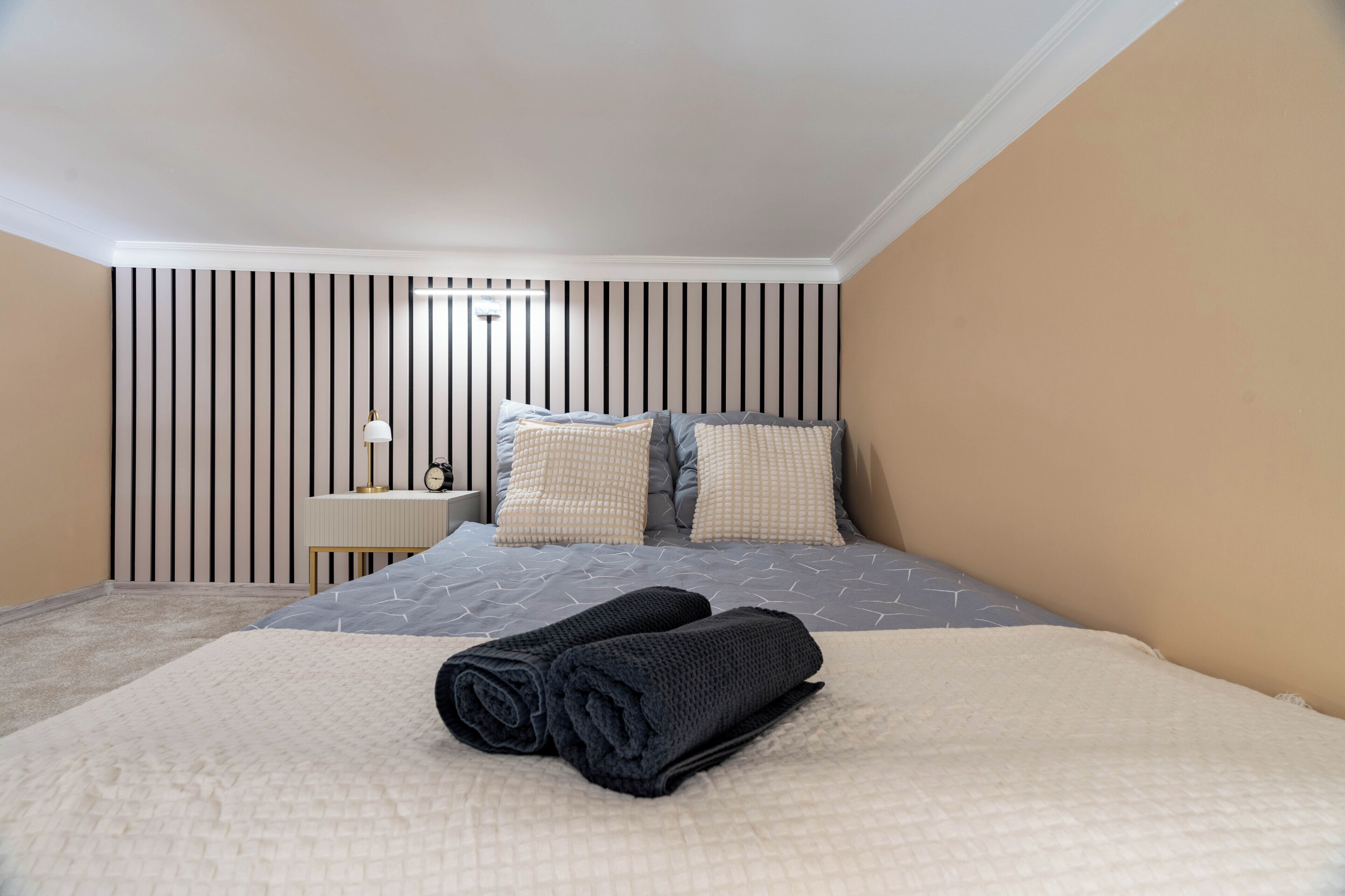 A bedroom with a bed, pillows, a bedside table, and a wall with vertical stripes.