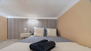 Un dormitorio con cama, almohadas, una mesita de noche y una pared a rayas verticales.