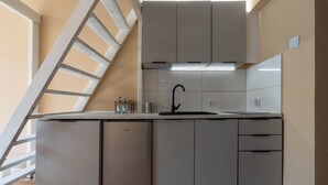 Una cocina compacta con lavavajillas integrado, un lavamanos y una escalera que lleva a un nivel superior.