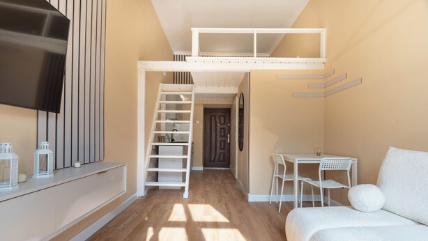 Una habitación moderna con literas, un televisor montado en la pared, una zona de comedor con mesa y sillas, y un sofá.