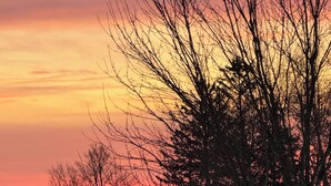Talo, jonka edessä on lumipeitteinen nurmikko ja jonka taustalla kohoavat paljaat puut auringonlaskun värittämää taivasta vasten.