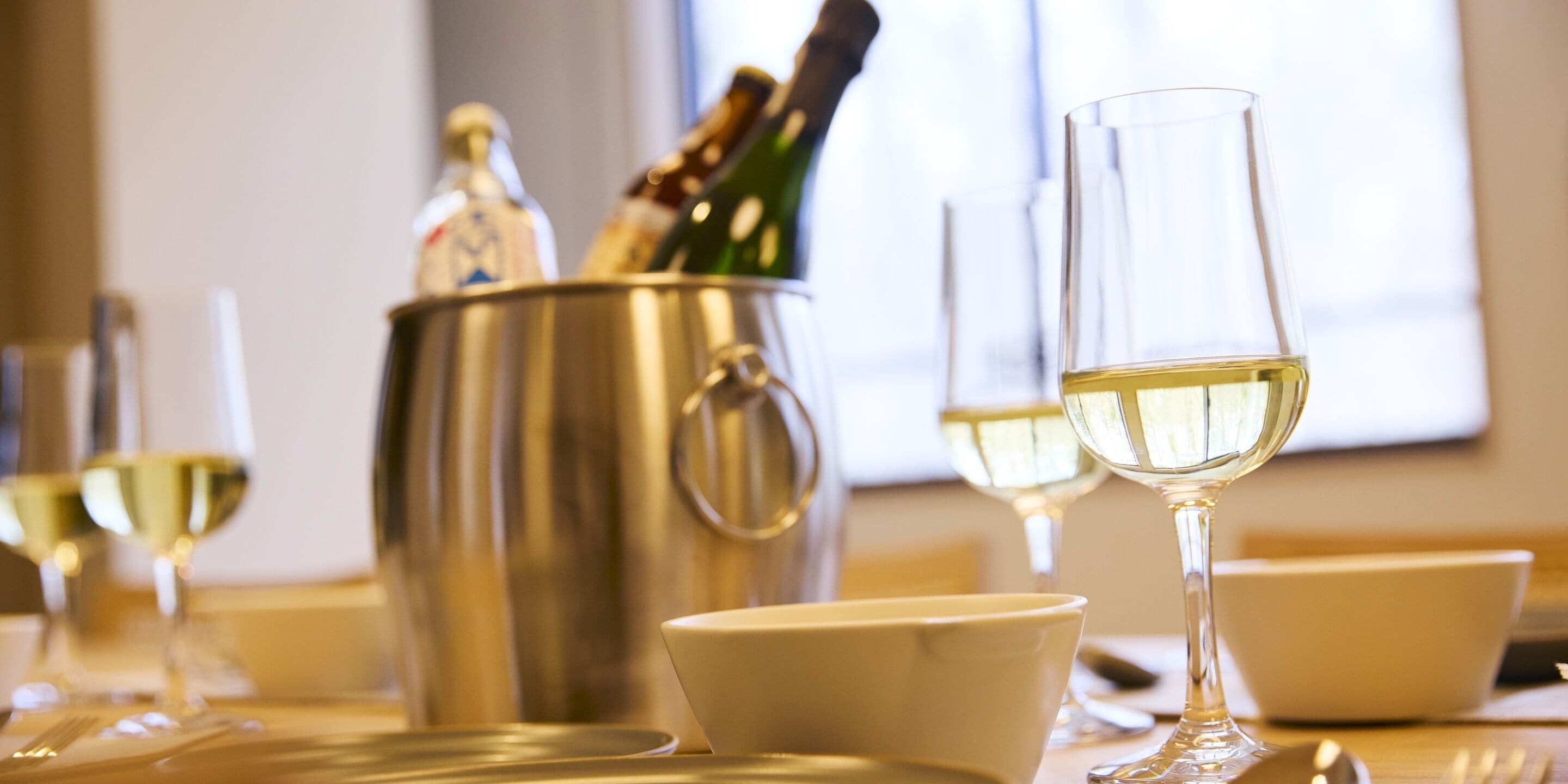 Ein Esstisch mit Weingläsern, einer Champagnerflasche und einem Metallbehälter.
