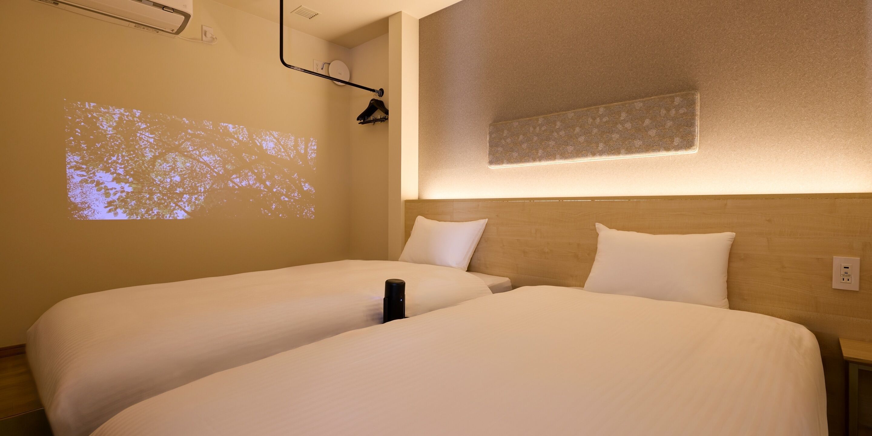 A hotel room with two beds, a projector on the wall, and a wooden headboard.