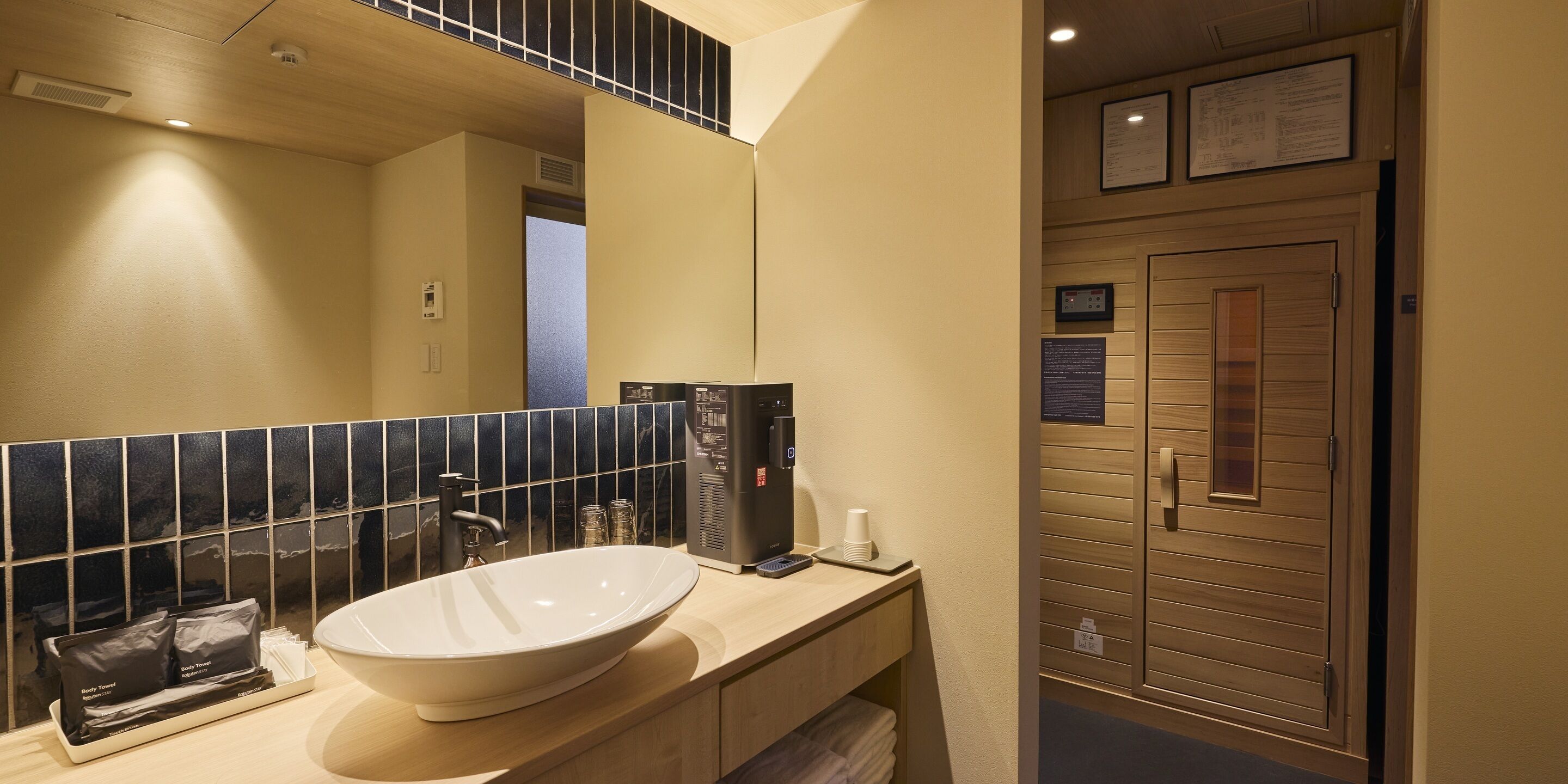 A bathroom with a large white sink, a mirror, a black tiled backsplash, a wooden door, and a small shelf with toiletries.