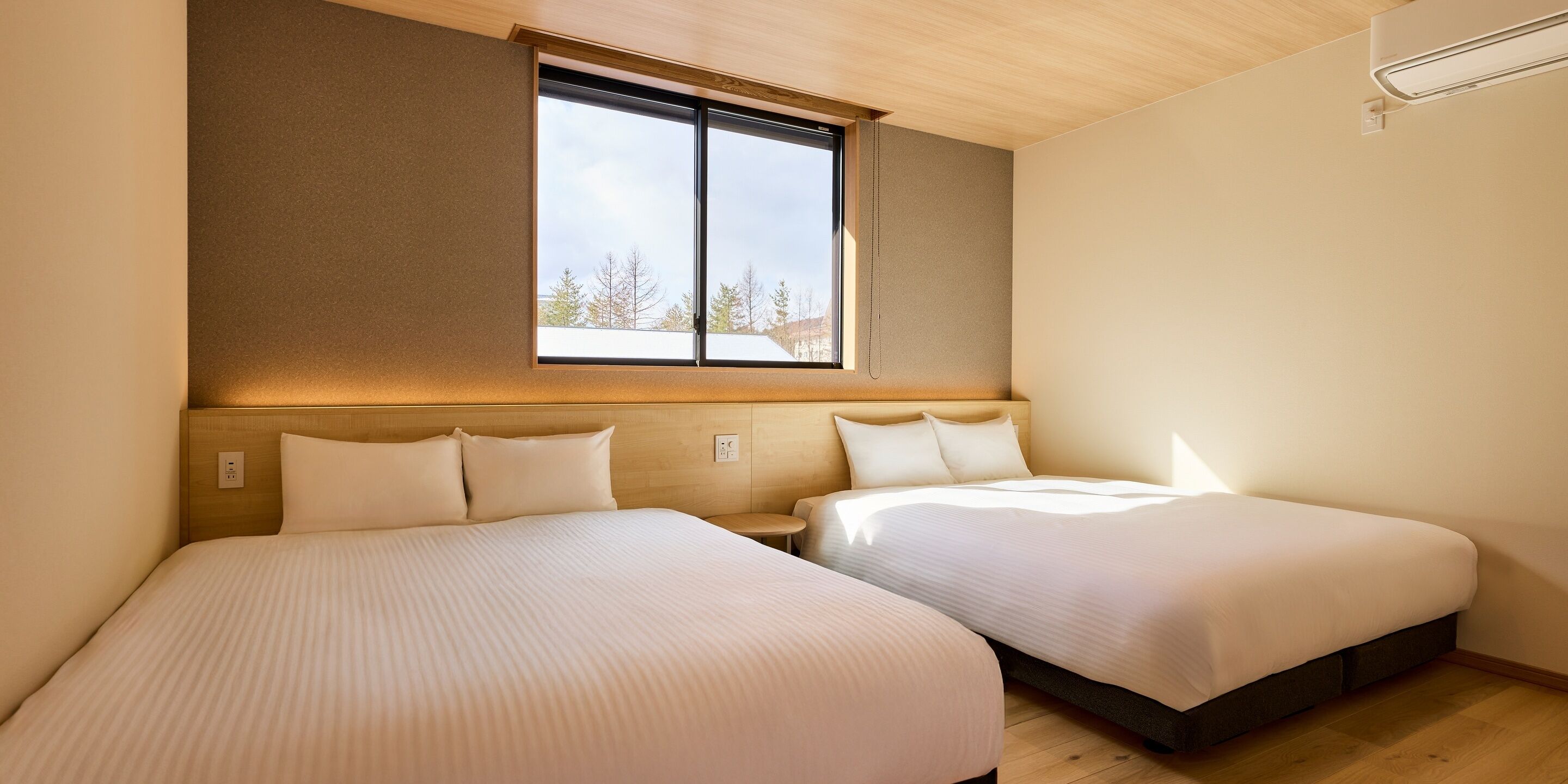 Une chambre d’hôtel avec deux lits, une grande fenêtre et un plafond en bois.