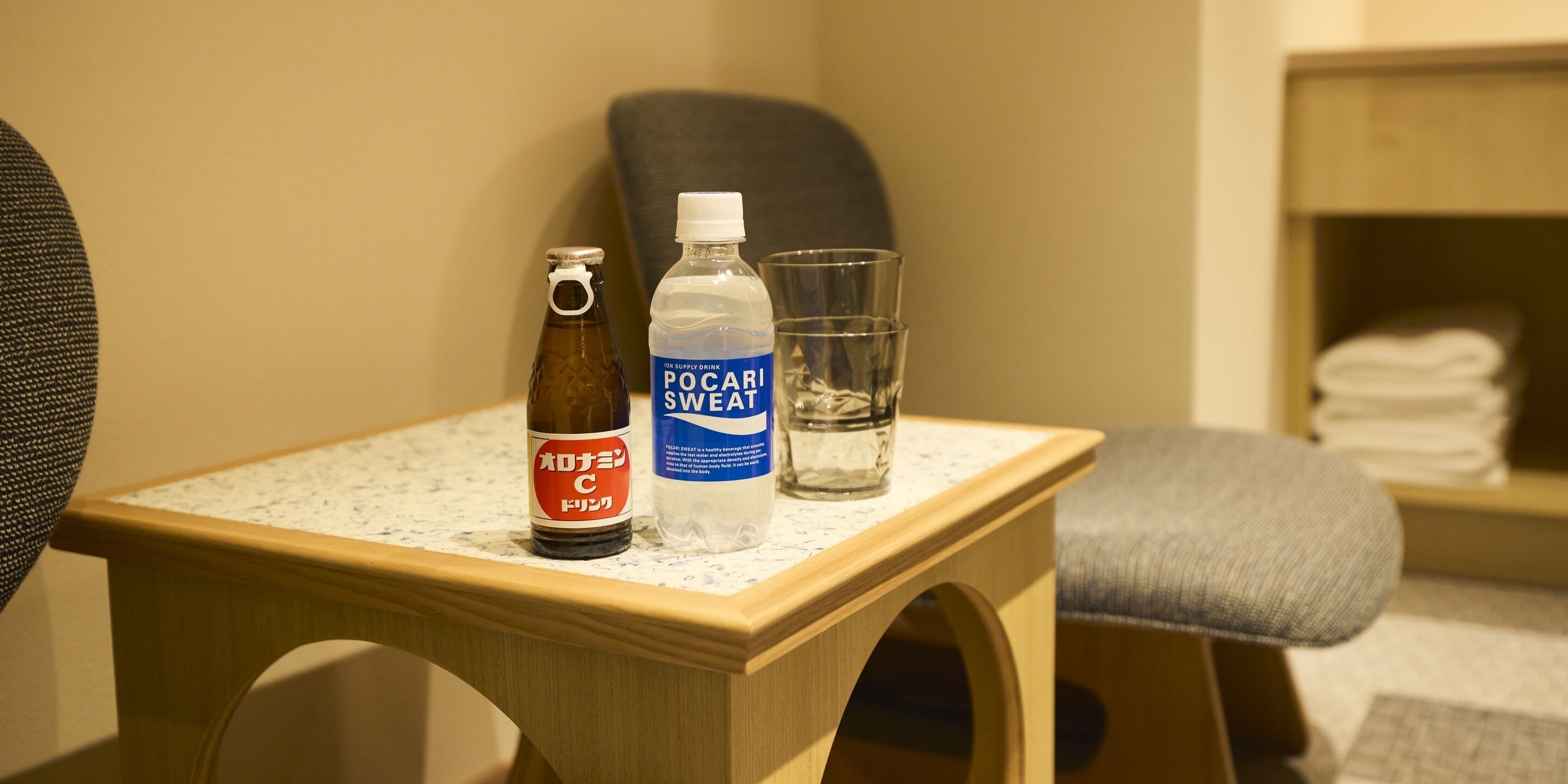 Una pequeña mesa de madera con una botella de Pocari Sweat, una botella de Coca-Cola y un vaso de agua.