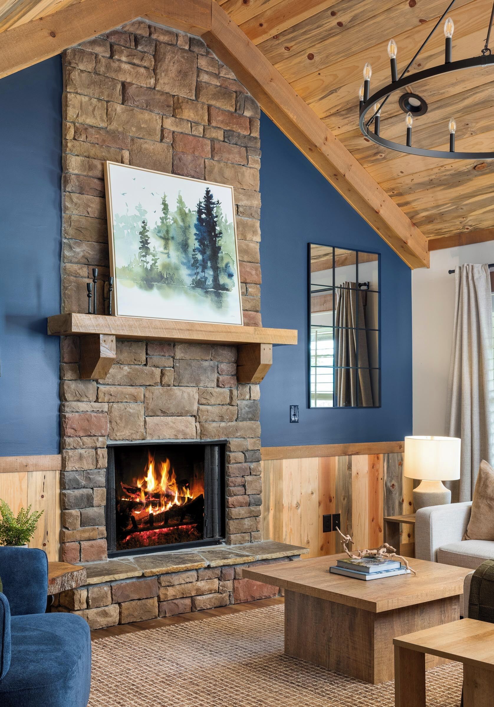 Une cheminée en pierre avec un feu de bois, un mur bleu, un plafond en bois et un lustre.
