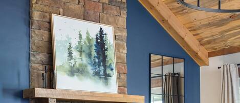Une cheminée en pierre avec un feu de bois, un mur bleu, un plafond en bois et un lustre.