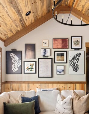 A room with a wooden ceiling, a ceiling light fixture, and a wall adorned with framed artwork.
