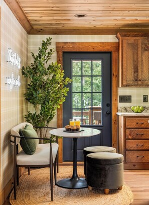 A cozy kitchen with a wooden door, a dining table with chairs, and a potted plant.