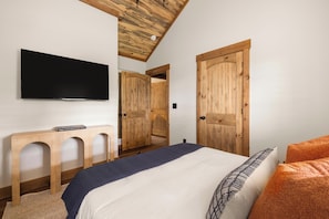 A bedroom with a bed, a TV, wooden doors, and a ceiling with exposed beams.