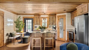 Eine moderne Küche mit Holzschnitzereien, einer zentralen Kochinsel mit Barhocker, einem Kühlschrank und einem Essbereich mit Tisch und Stühlen.