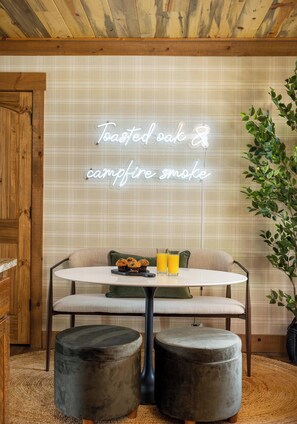 A cozy dining area with a neon sign, a round table, two chairs, and a potted plant.