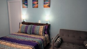 Un dormitorio con cama, dos lámparas de pared, una mesita de noche, una silla y tres cuadros enmarcados.