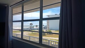 Una ventana con vista a la playa, un edificio blanco y vehículos estacionados.