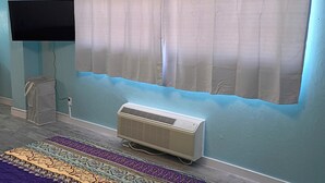 Una habitación con una televisión de pantalla plana montada en la pared, aire acondicionado y una alfombra estampada en el suelo.