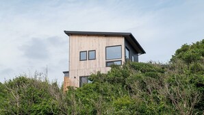 Un bâtiment moderne à deux étages, doté d’une façade en bois et de grandes fenêtres, entouré d’une végétation luxuriante.