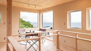 Un intérieur moderne avec un plafond en bois, de grandes fenêtres offrant une vue sur la mer et un coin repas avec une table et des chaises.