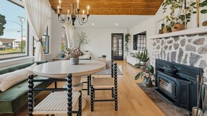 A cozy living room with a round dining table, a green sofa, a fireplace, and large windows.