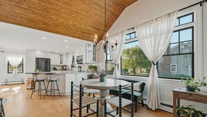 A modern kitchen with white cabinets, a round dining table with stools, and a wooden ceiling.