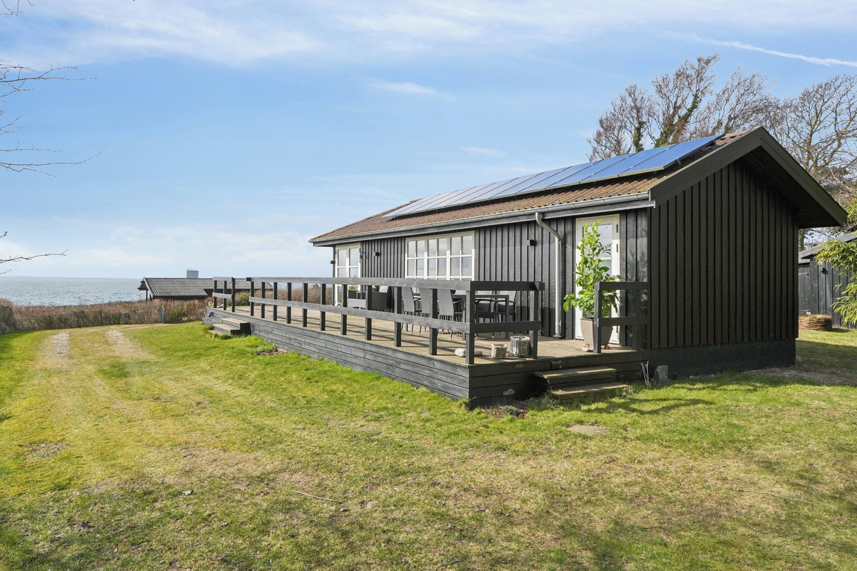 A wooden building with a deck, large windows, and a solar panel on the roof.