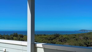 A balcony with a view of the ocean and a distant landmass. - Ocean View Retreat (Magenta)