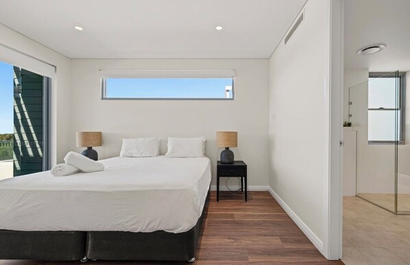 A modern bedroom with a large bed, two bedside tables, a window, and a door leading to a bathroom.