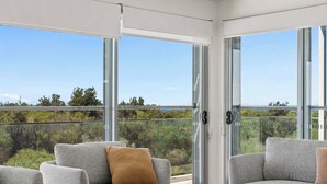 A balcony with a glass door, grey sofas, and a view of greenery. - Ocean View Retreat (Magenta)