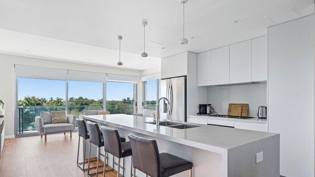 A modern kitchen with a large island, bar stools, and a view of the outdoors. - Ocean View Retreat (Magenta)