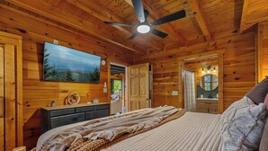 Een slaapkamer in een houten chalet met een bed, een plafondventilator, een bevestigde televisie en een houten dressoir.