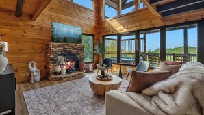 Een gezellig chalet interieur met een stenen openhaard, houten wanden en grote ramen met uitzicht op de natuur.