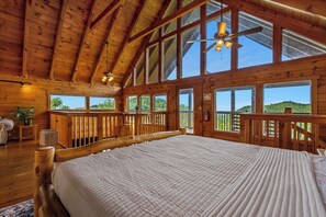 A spacious bedroom with a large bed, wooden ceiling beams, and large windows offering a view of the outdoors. - *New Panoramic Smoky Mtn Views-Mins to Dollywood (Sevierville)