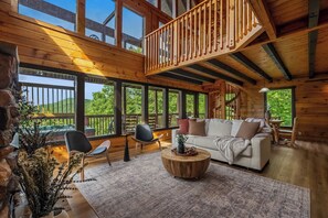 Un intérieur en bois avec un canapé, des fauteuils, une table basse ronde et de grandes fenêtres.