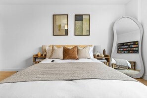 Un dormitorio ordenado con cama, mesitas de noche, un espejo grande y arte abstracto en la pared.