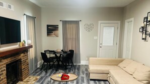 A living room with a fireplace, a sofa, a dining table with chairs, and a coffee table with a board game. - Cozy family friendly Entire Home l, 2BR,  Free Parking, 20min to Minneapolis (Champlin)