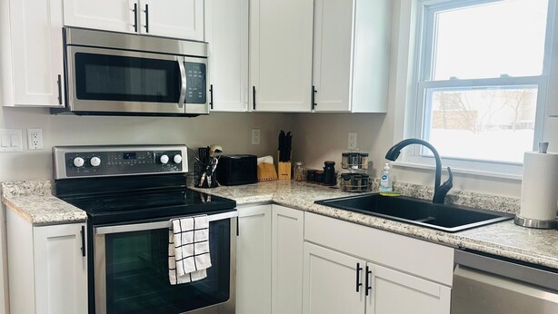 A modern kitchen with white cabinets, a stainless steel oven, a microwave, a sink, and a window providing natural light. - Cozy family friendly Entire Home l, 2BR,  Free Parking, 20min to Minneapolis (Champlin)