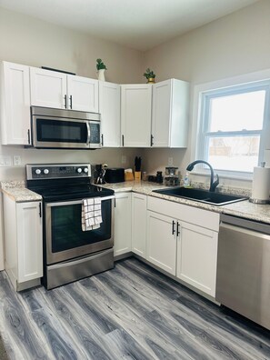 A modern kitchen with white cabinets, a stainless steel oven, a microwave, a sink, and a window providing natural light. - Cozy family friendly Entire Home l, 2BR,  Free Parking, 20min to Minneapolis (Champlin)