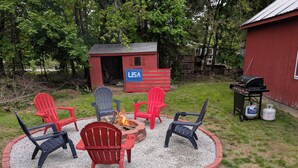 En rund sittgrupp med Adirondack-stolar, en eldstad och en grill.