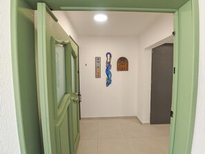 Un couloir avec des portes vertes, un sol carrelé et deux éléments décoratifs sur les murs.